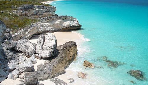 Description: An aerial view of a beach with turquoise water and rocky cliffs, offering breathtaking views of the Bahamas.
